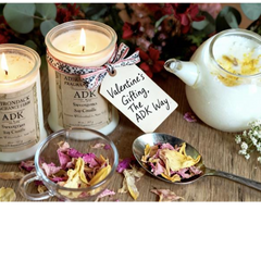 Candles with a teapot and dried flowers on a wooden surface, featuring 'ADK' branding.