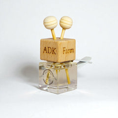 Small clear bottle with wooden cap and 'ADK Farm' branding on a white background